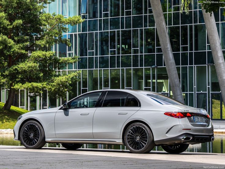 Silver luxury sedan side view parked by a glass office building